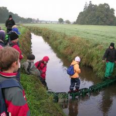 Kinder überqueren den Fluss Haaren bei Oldenburg. Es wurde eine Brücke aus umgedrehten Getränkekisten in den Fluss gestellt über die die Kinder gehen.