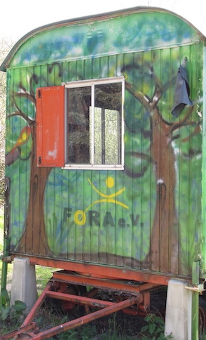Stirnseite eines Bauwagens mit Deixel und Fenster. Unterhalb des Fensters ist das Foralogo. Auf dem Bauwagen wurde ein Wald gemalt.